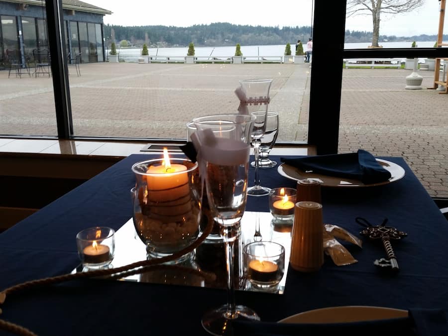 Een gedekte tafel met kaarsen, glazen en bestek, met uitzicht op een meer.