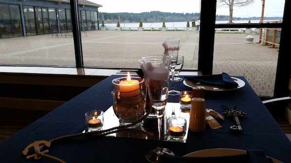 Mesa dispuesta con velas, copas y cubiertos, con vistas a un lago.