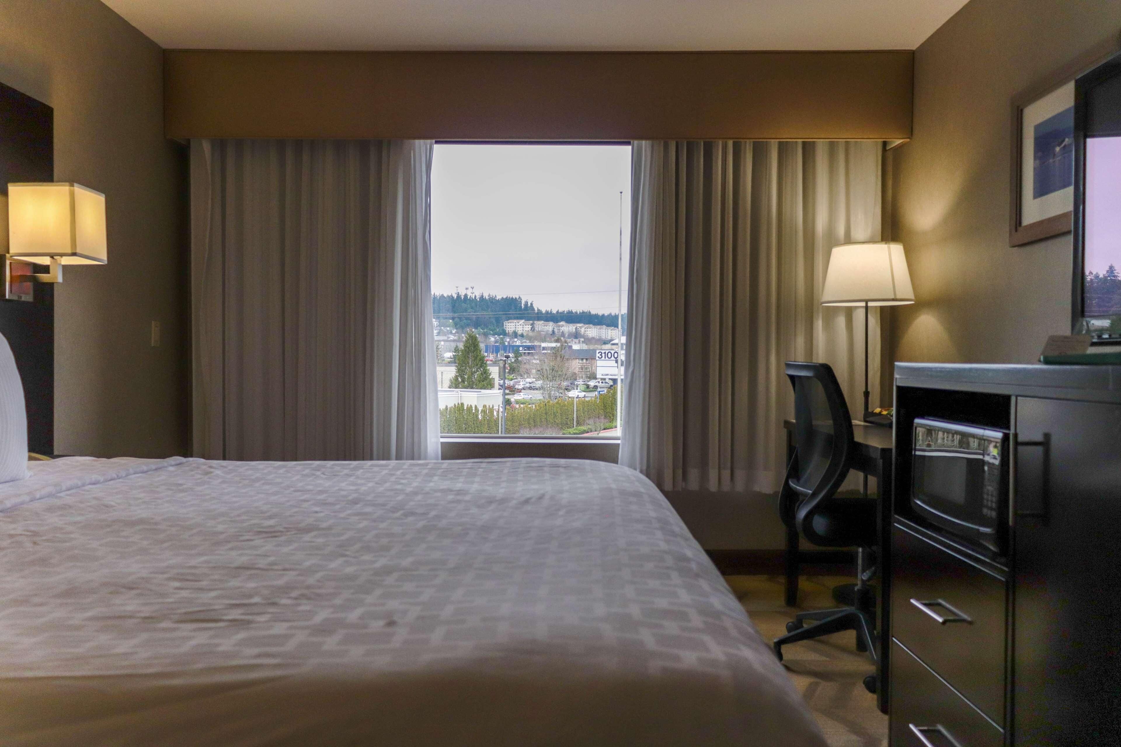 Una habitación de hotel con una cama grande, un escritorio con computadora, un microondas y vistas a un paisaje urbano por la ventana.