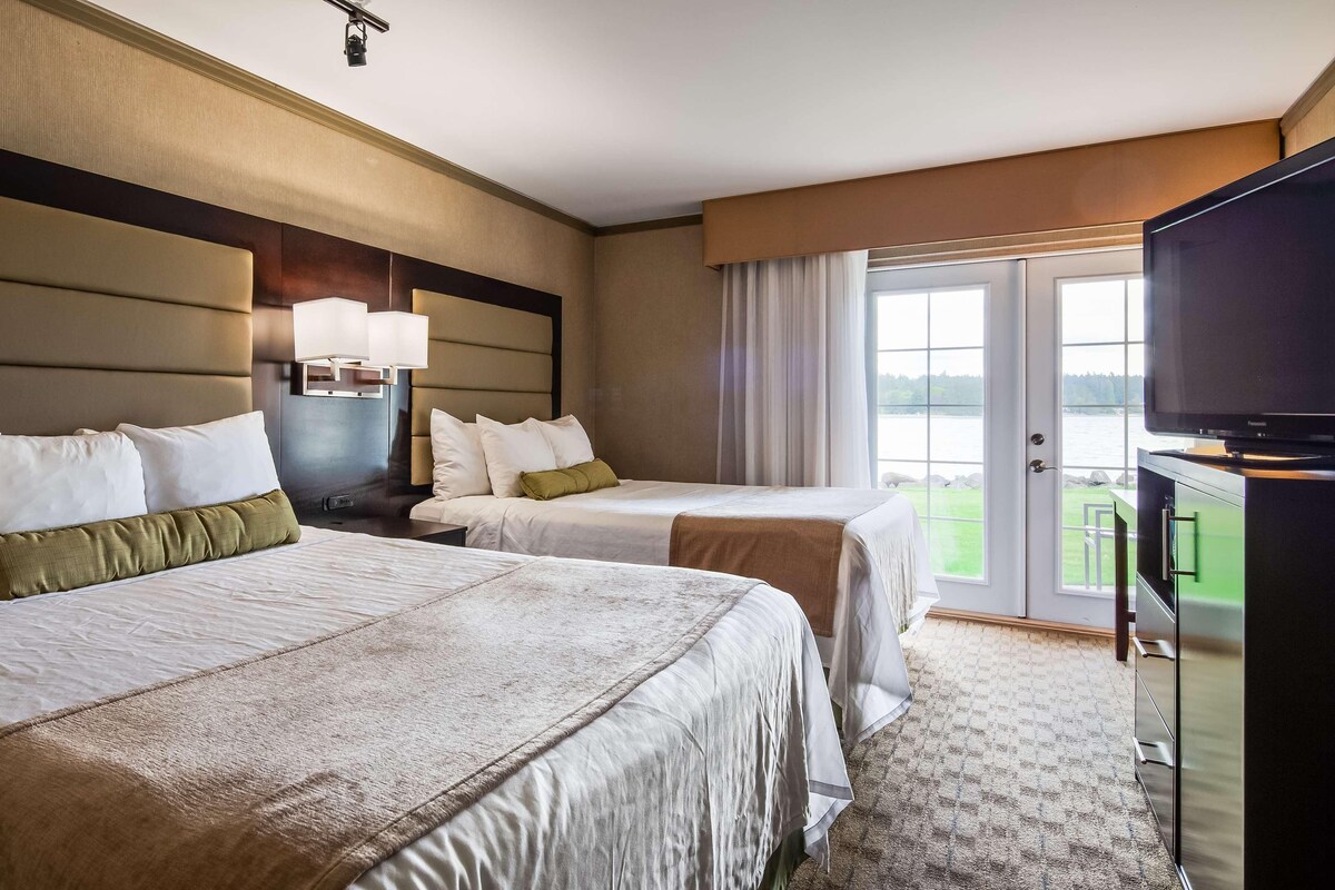 A hotel room with two beds, a television, and a view of a body of water.