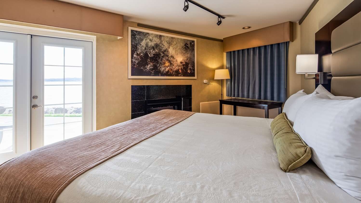 Habitación de hotel con una cama grande, chimenea, escritorio y vistas al exterior.