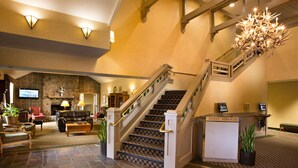 A grand lobby with a stone fireplace, a staircase with a chandelier, and a guest services desk.