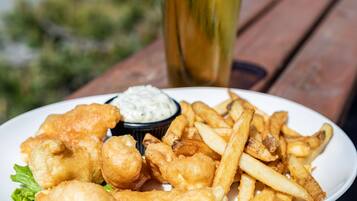 Un plato de pescado con papas fritas, salsa tártara y una cerveza en una mesa de madera.