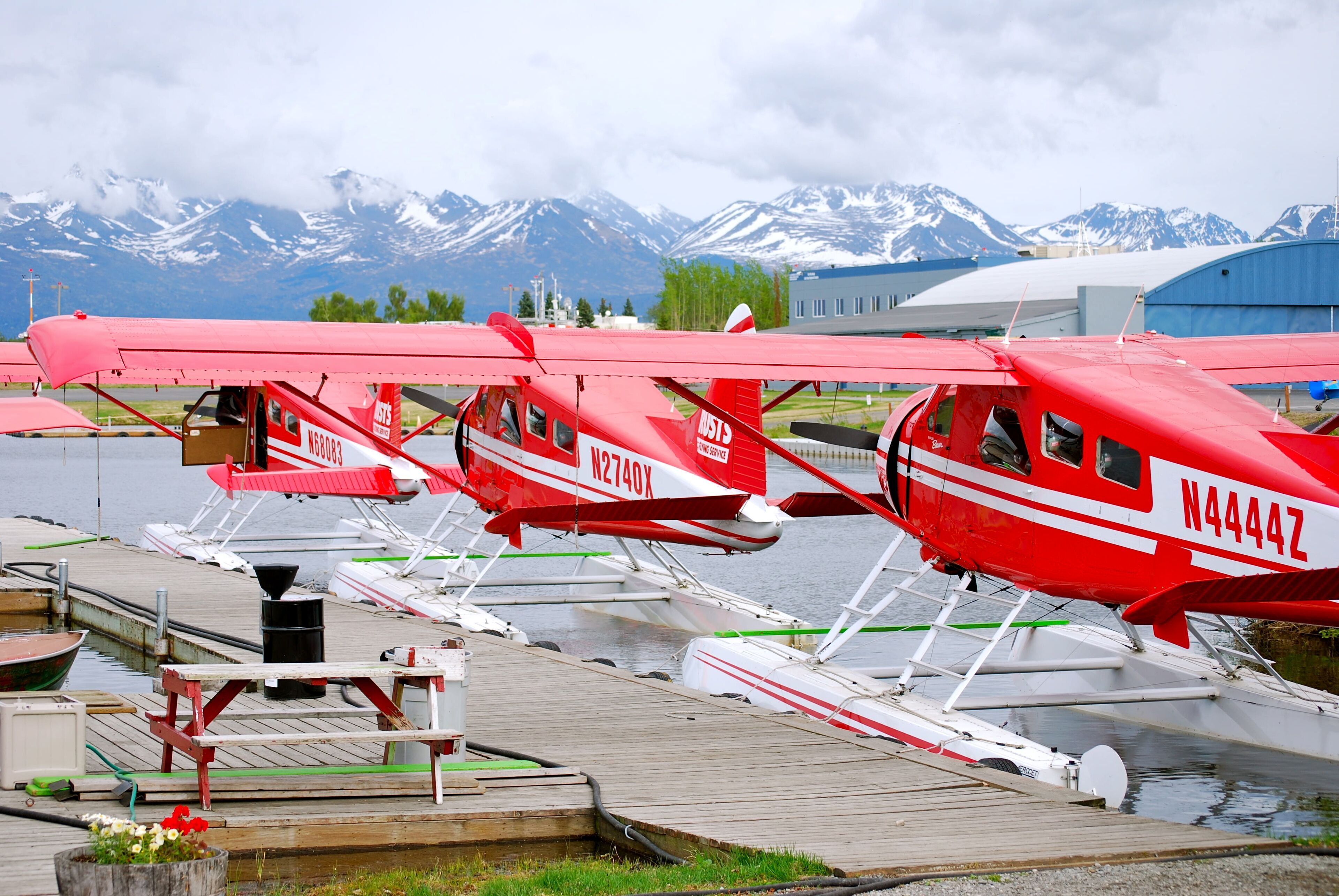 A row of red seaplanes docked at a wooden pier with mountains in the background.