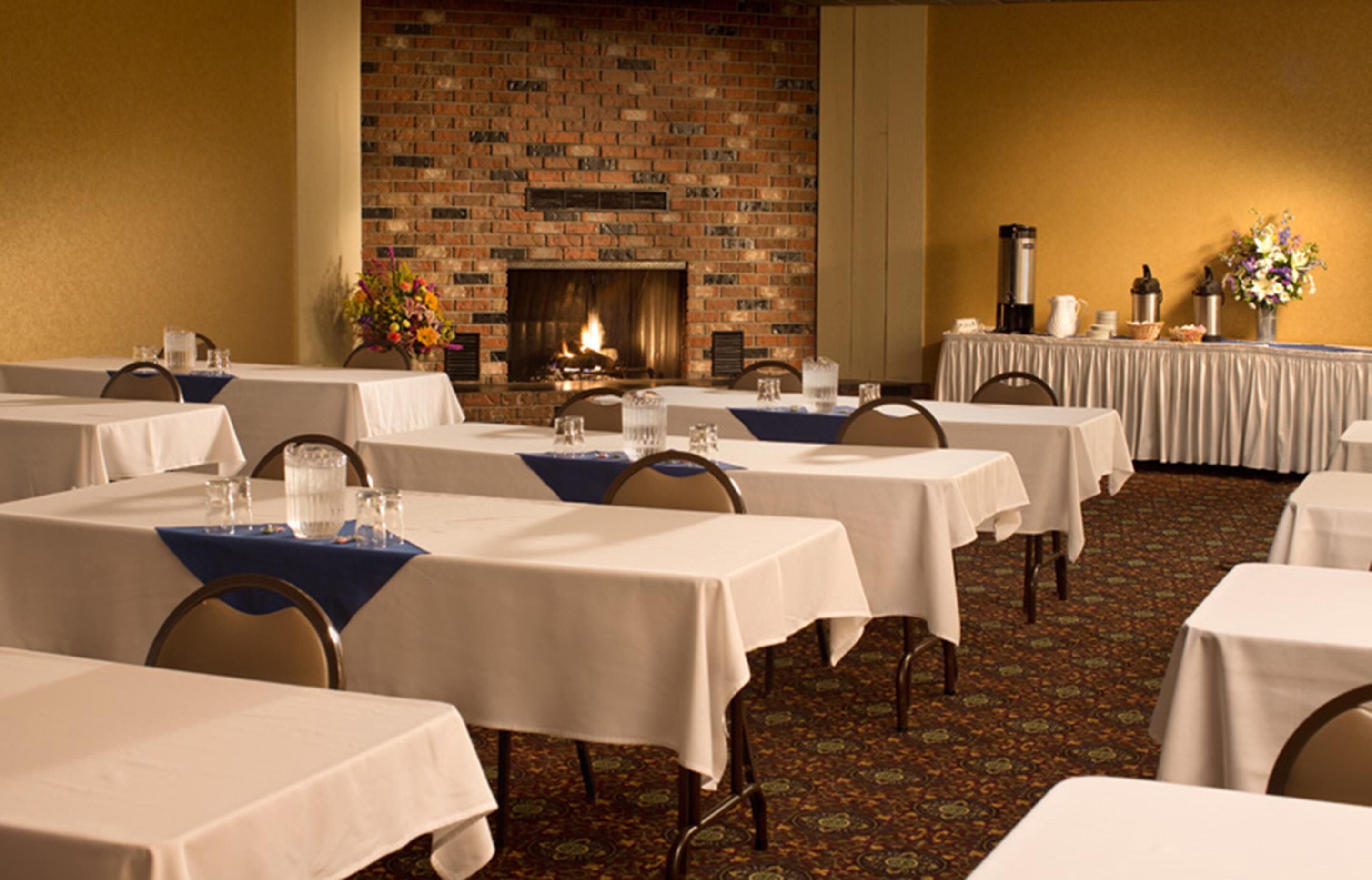 A conference room with multiple tables, a brick fireplace, and a carpeted floor.