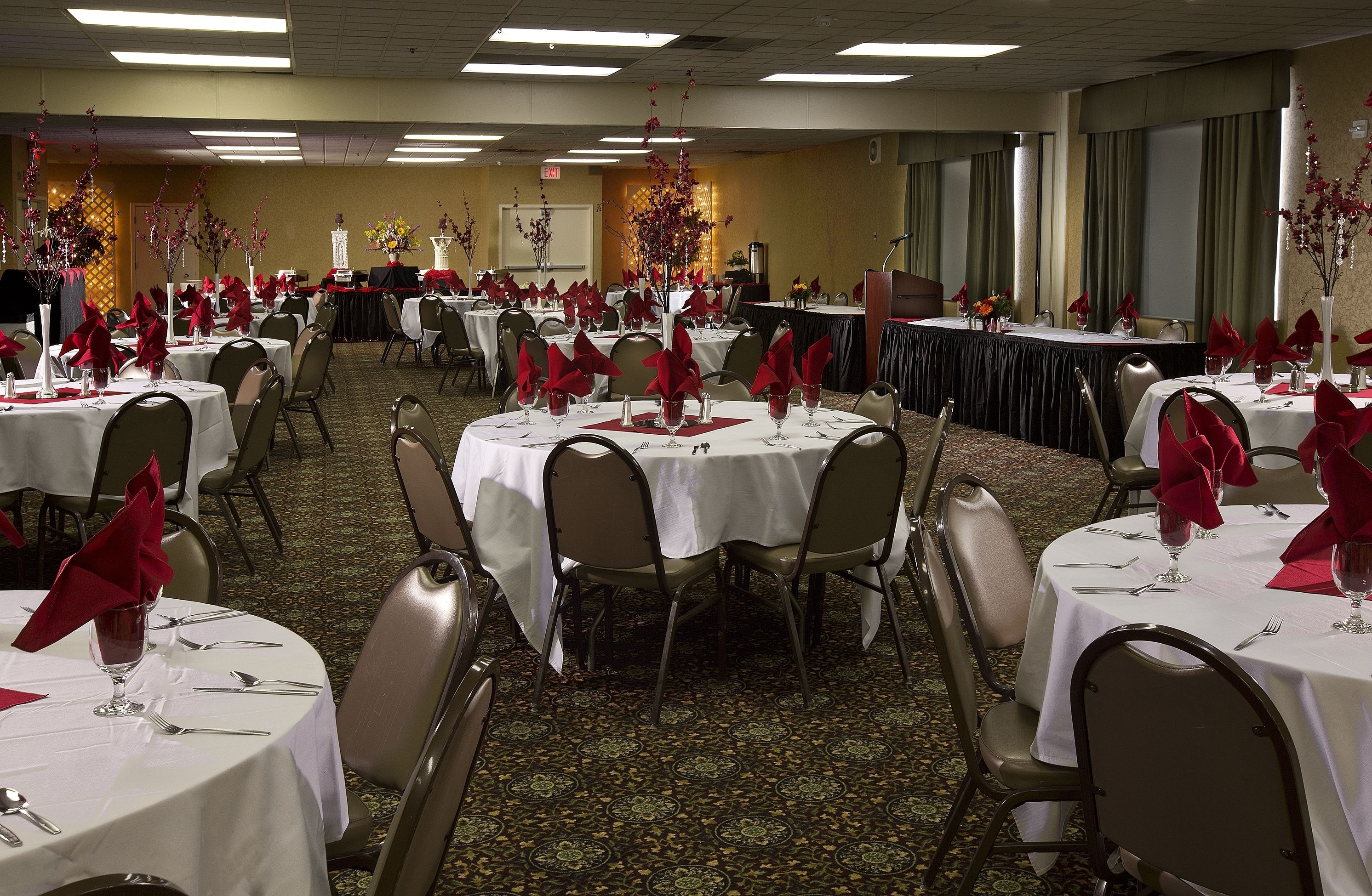 A banquet hall with round tables set for dining, each with white tablecloths, red napkins, and silverware.
