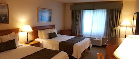 A hotel room with two beds, a desk, a chair, a lamp, an air conditioner, and a painting on the wall.