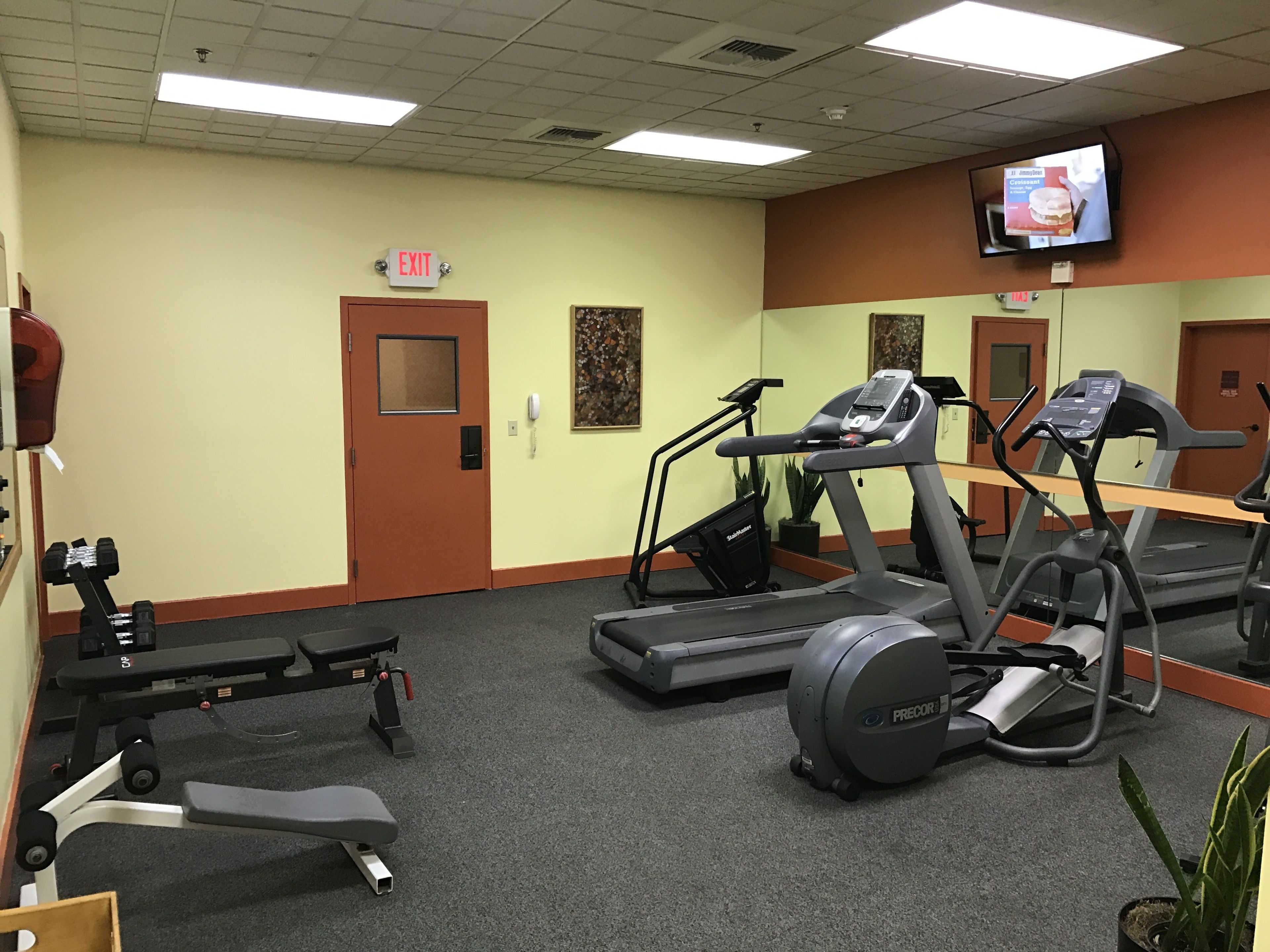 Un gimnasio con cintas de correr, una prensa de banca y un televisor montado en la pared.