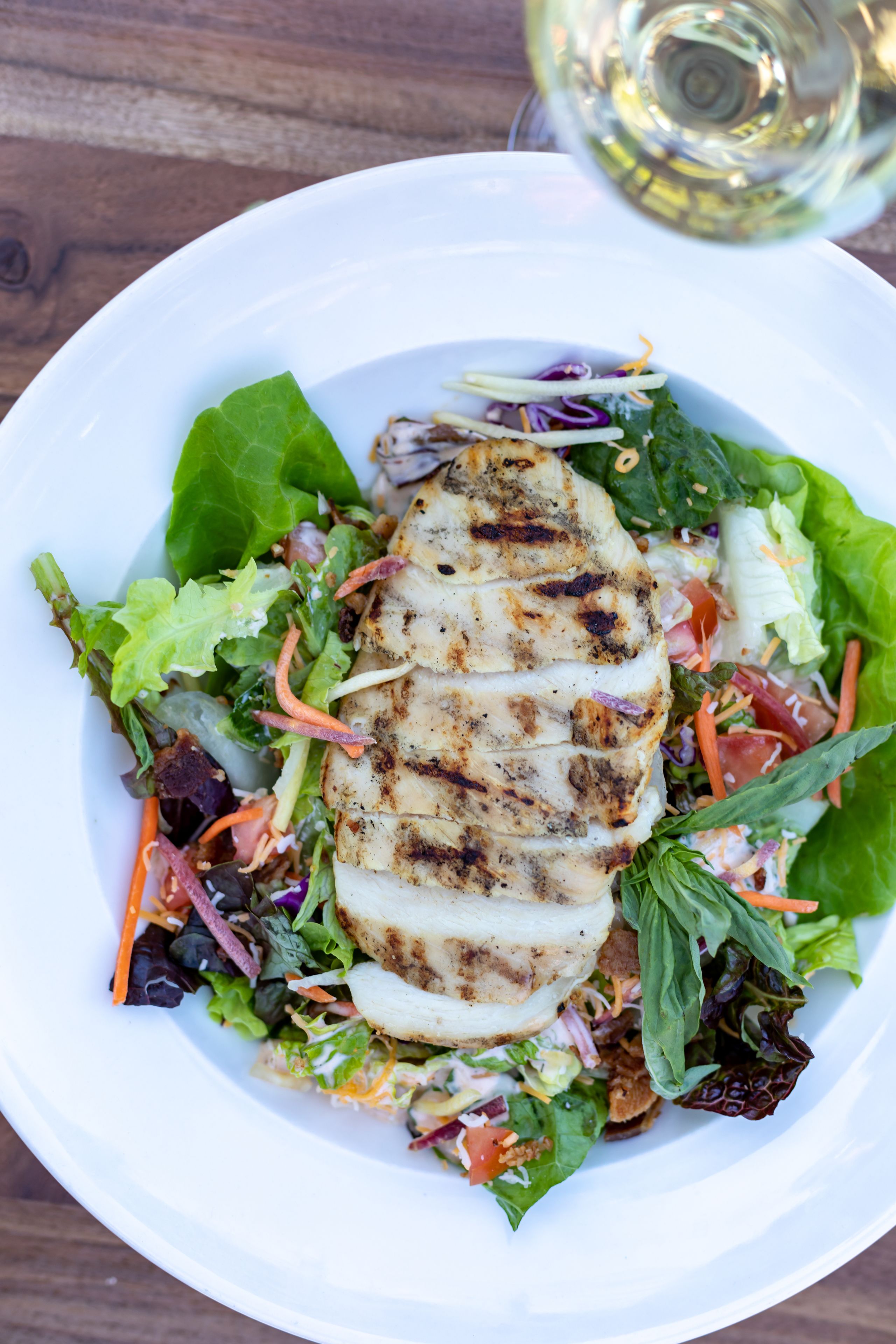 Un plato con pollo a la parrilla y una ensalada de lechugas variadas.
