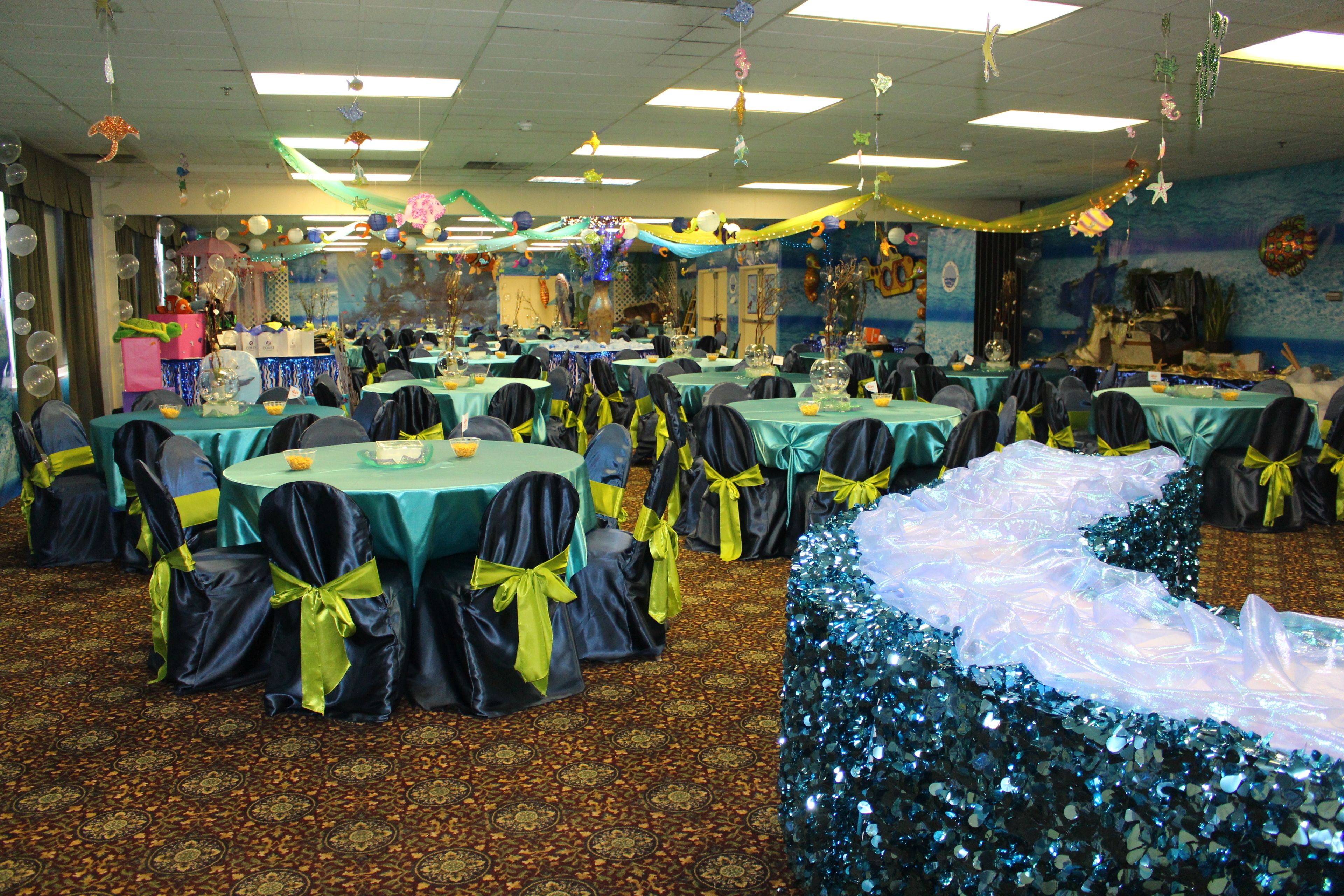 A banquet hall with round tables, chairs, and a decorative backdrop.