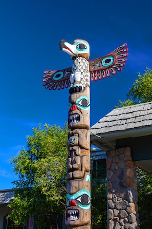 A totem pole with intricate carvings and a stone building in the background.