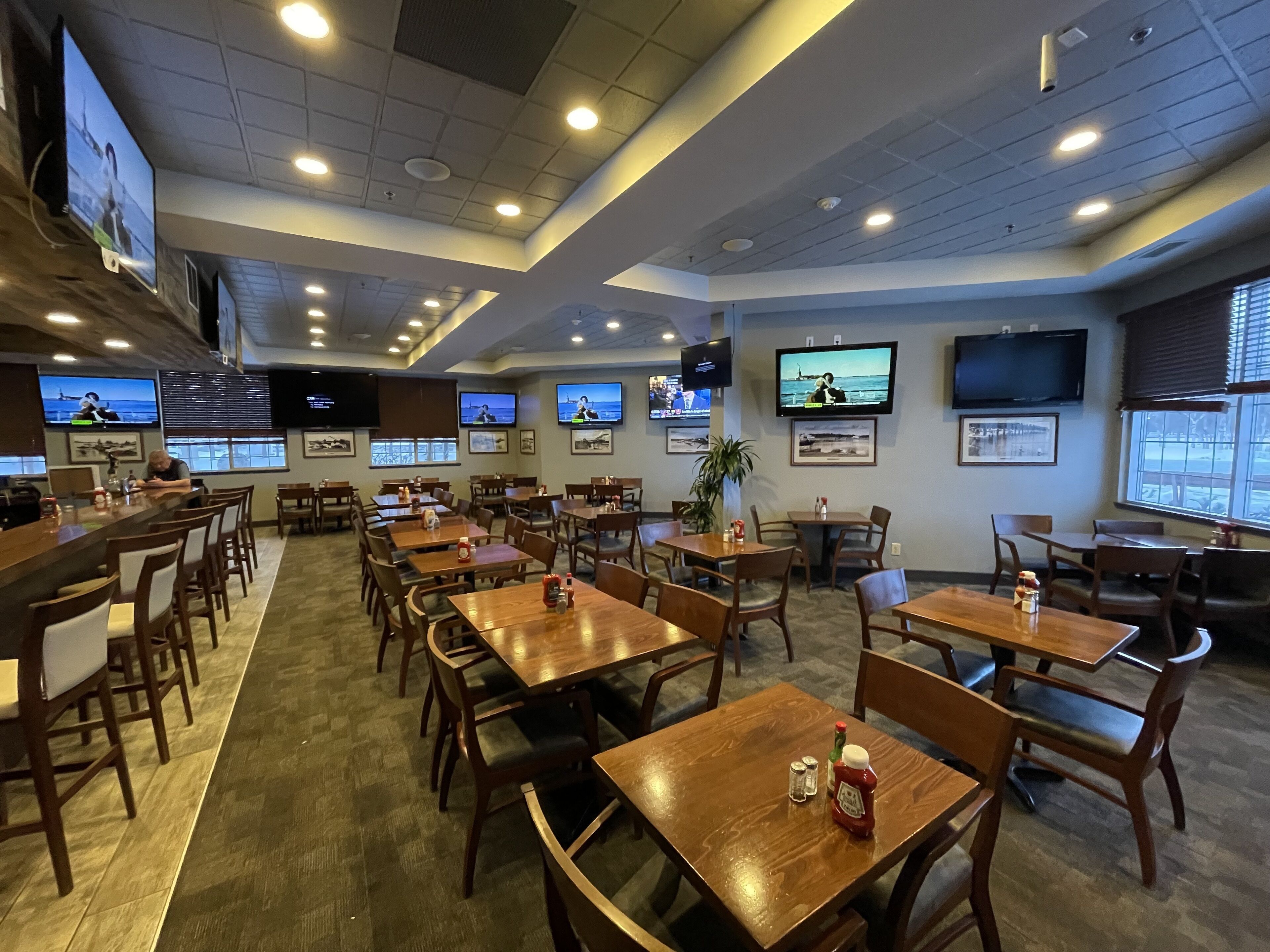 A restaurant with multiple tables and chairs, ceiling lights, and wall-mounted TVs displaying sports events.