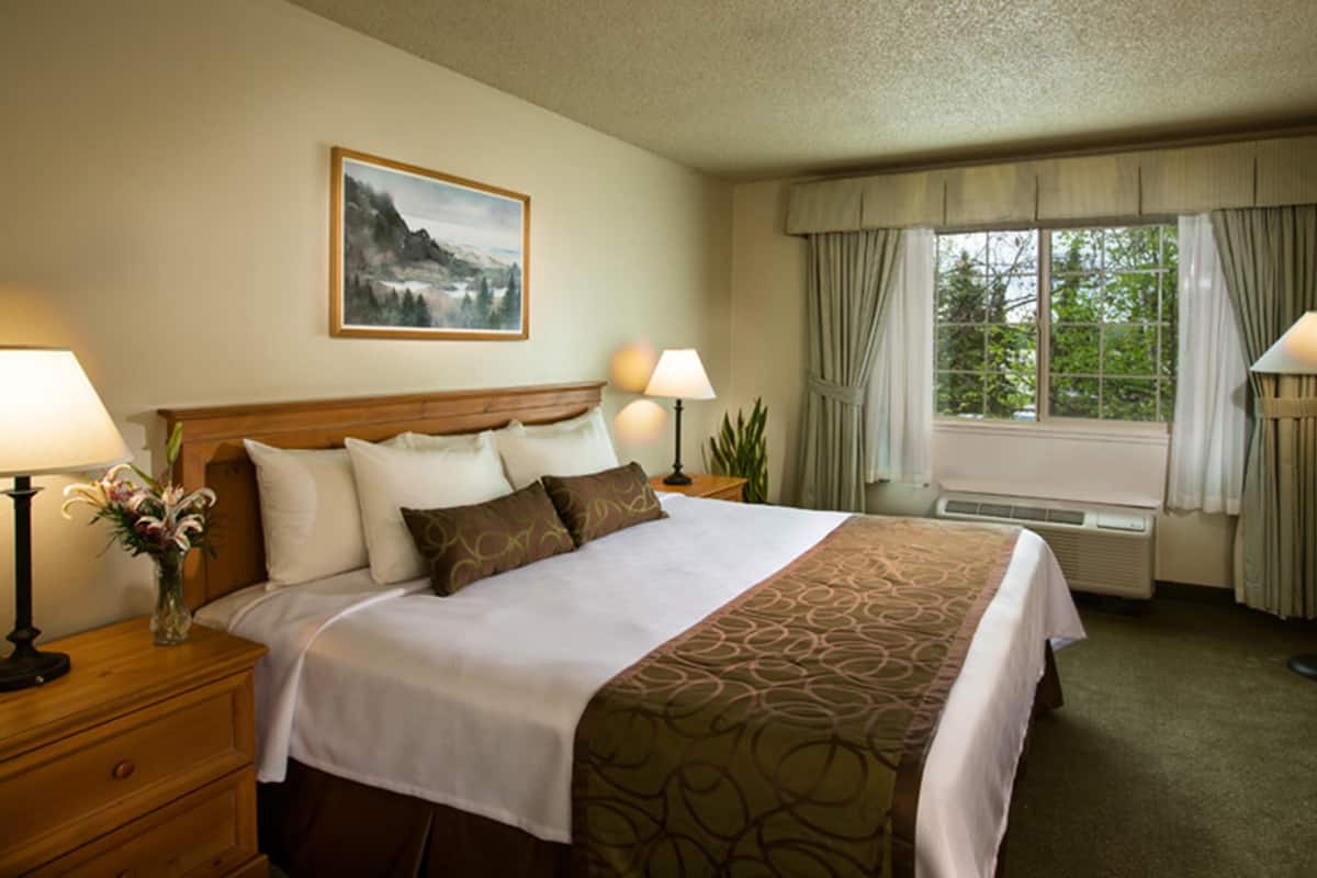 A hotel room with a large bed, two bedside tables with lamps, a window with curtains, and a painting on the wall.