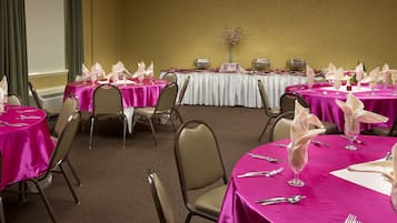 A conference room with multiple tables, each covered with a pink tablecloth and equipped with glassware and cutlery.