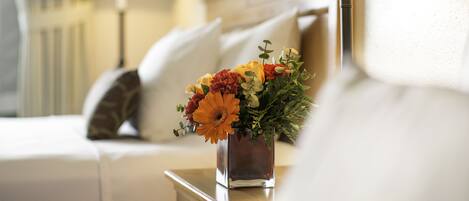 Ein ordentlich eingerichtetes Hotelzimmer mit einem Bett, einem Nachttisch mit Lampe und einem Blumenstrauß.