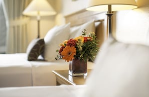 A neatly arranged hotel room with a bed, a bedside table with a lamp, and a vase of flowers.