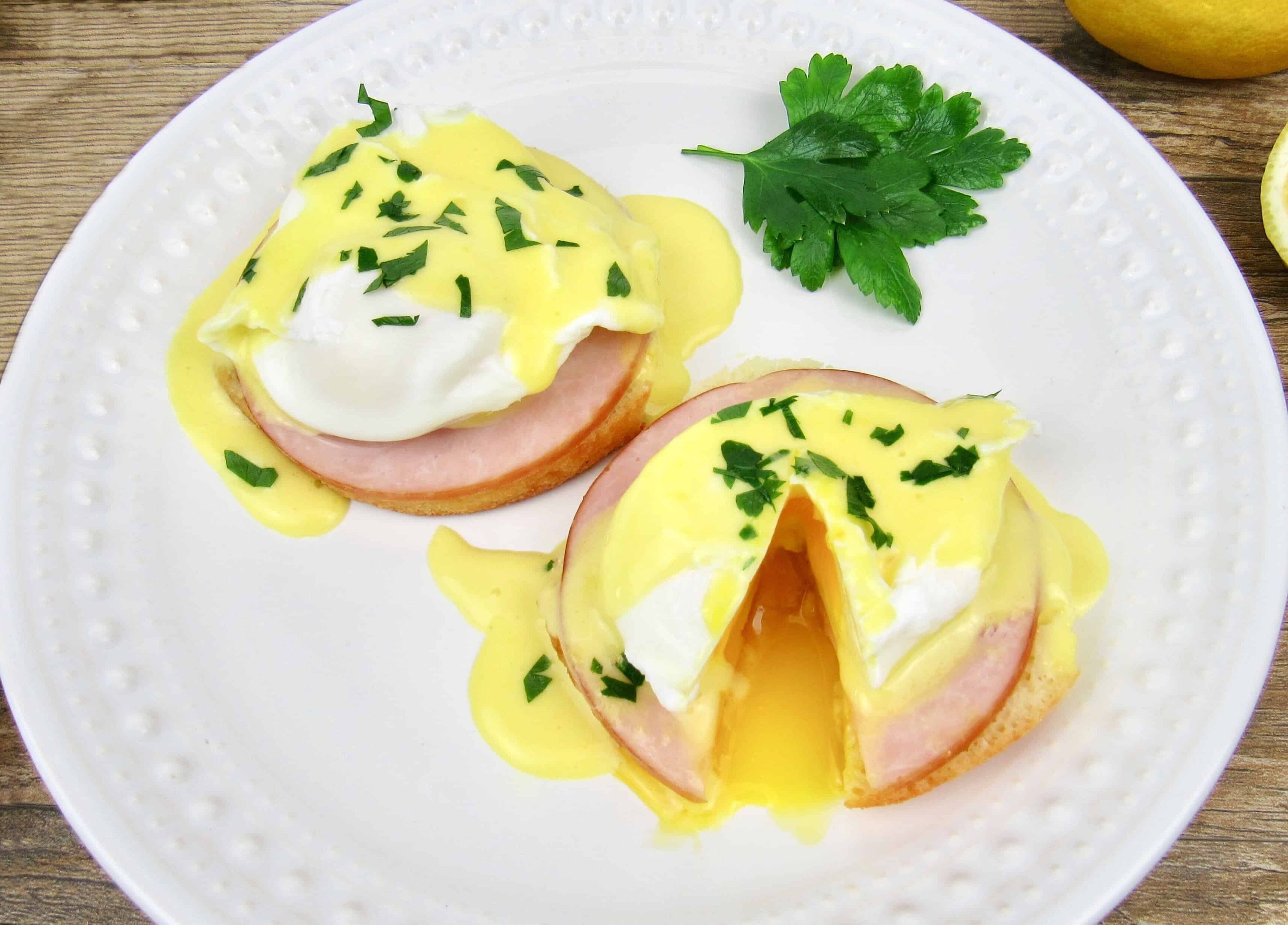 Two eggs benedict sandwiches on a white plate with parsley garnish.