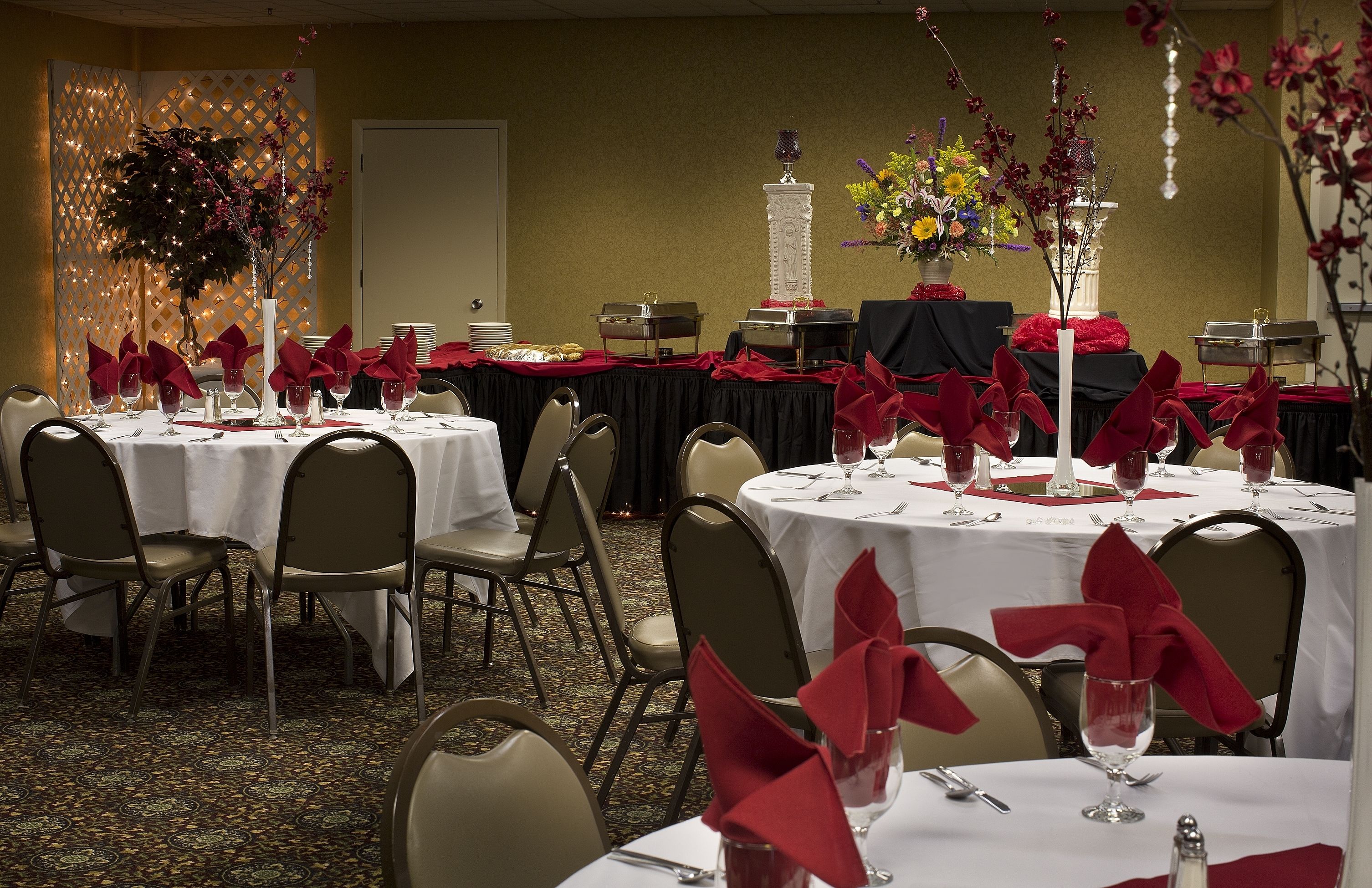 A banquet hall with round tables set for dining, each with white tablecloths and red napkins.