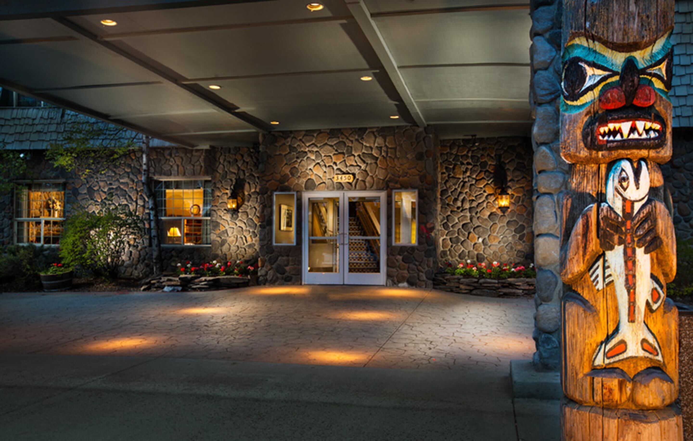 A stone building with a wooden totem in front, a stone wall, and a glass door entrance.
