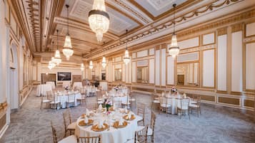 Un gran espai de banquet amb un sostre decorat i candelabres, taules rodones preparades per a dinar i una disposició àmplia.