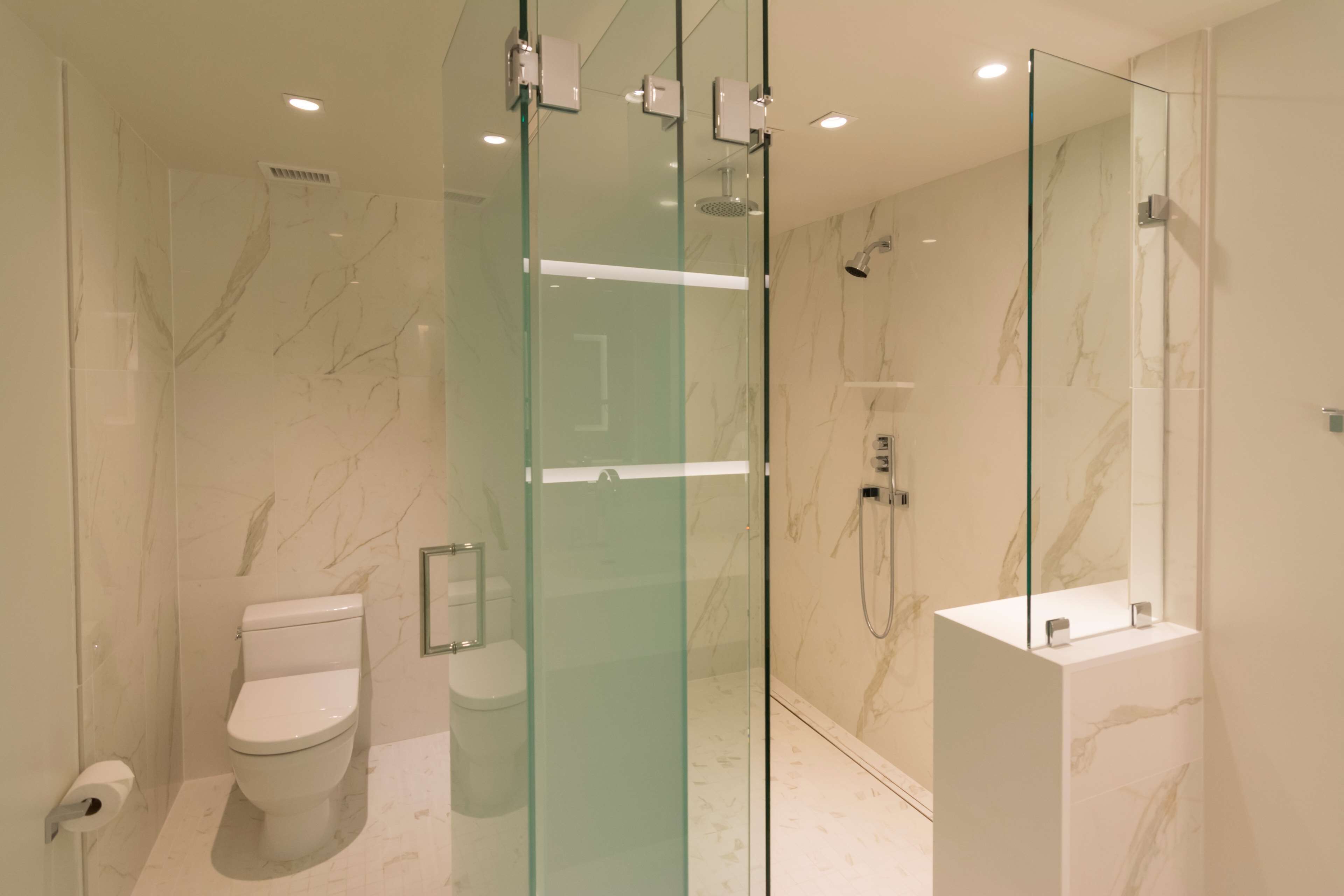 Un baño moderno con ducha de vidrio, inodoro y un espejo grande.