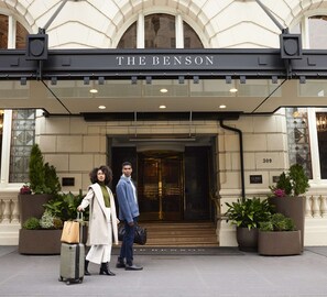 The entrance of The Benson hotel with a classic facade, a grand staircase, and potted plants.