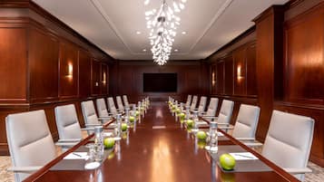 A conference room with a long table, white chairs, and a chandelier.