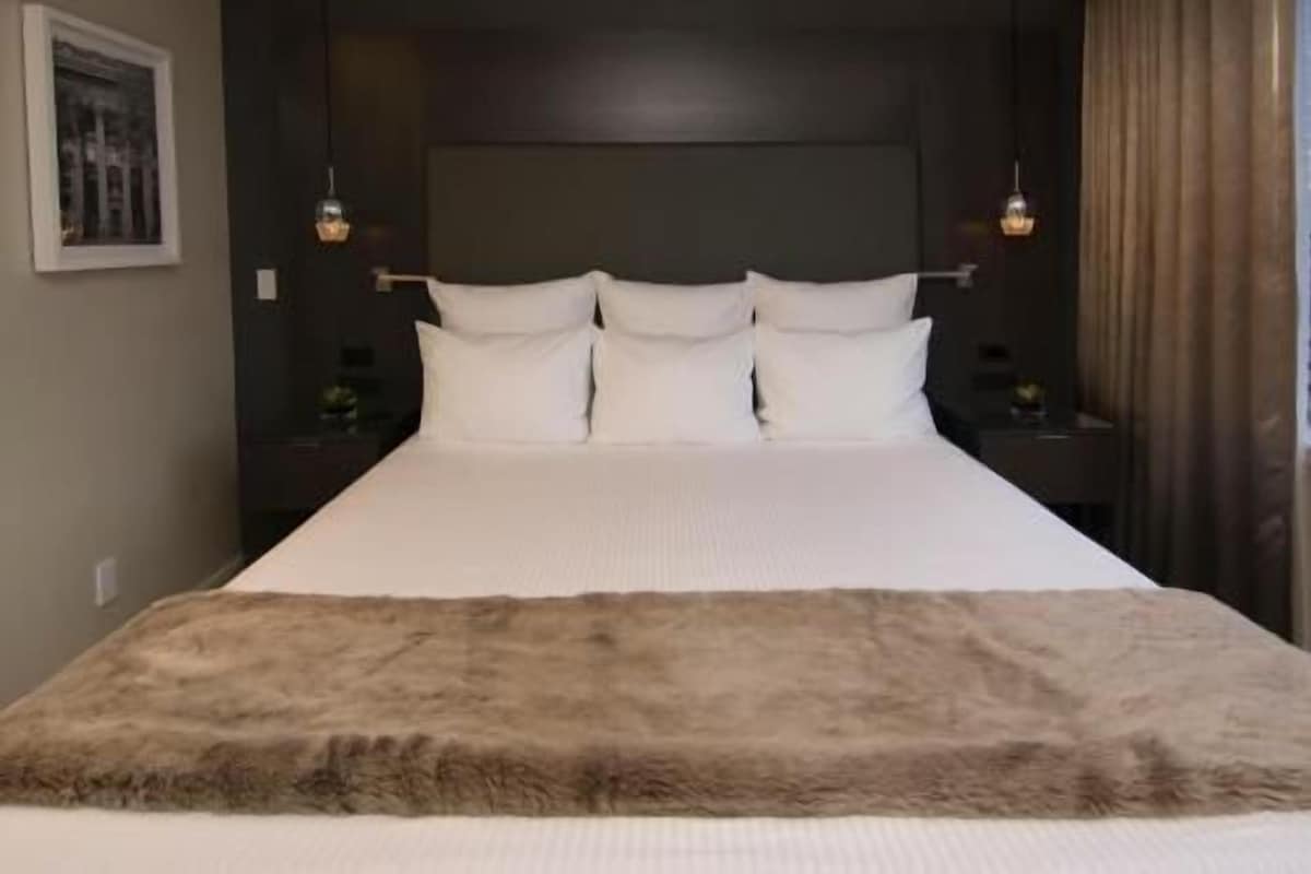 Un lit avec du linge de lit blanc et un plaid en fourrure, une tête de lit sombre et deux lampes de chevet.