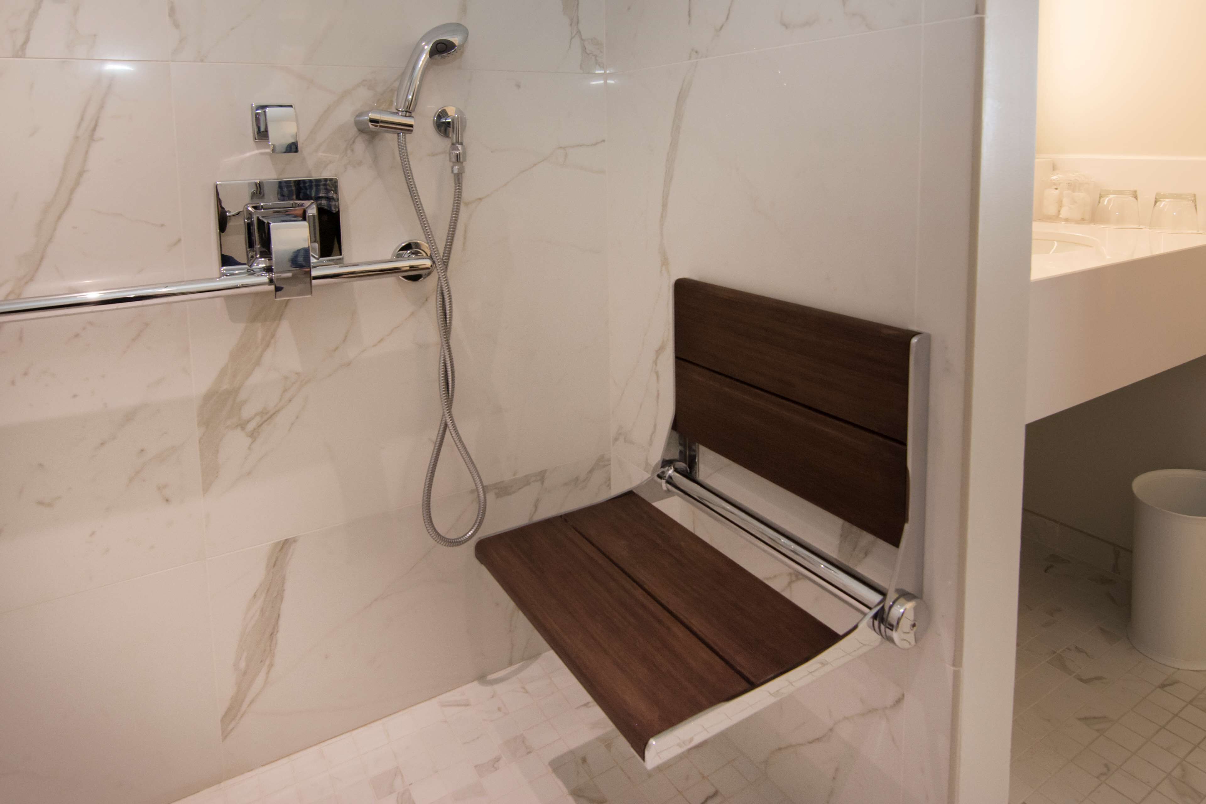 A bathroom with a shower, a wooden shelf, and a marble-tiled wall.