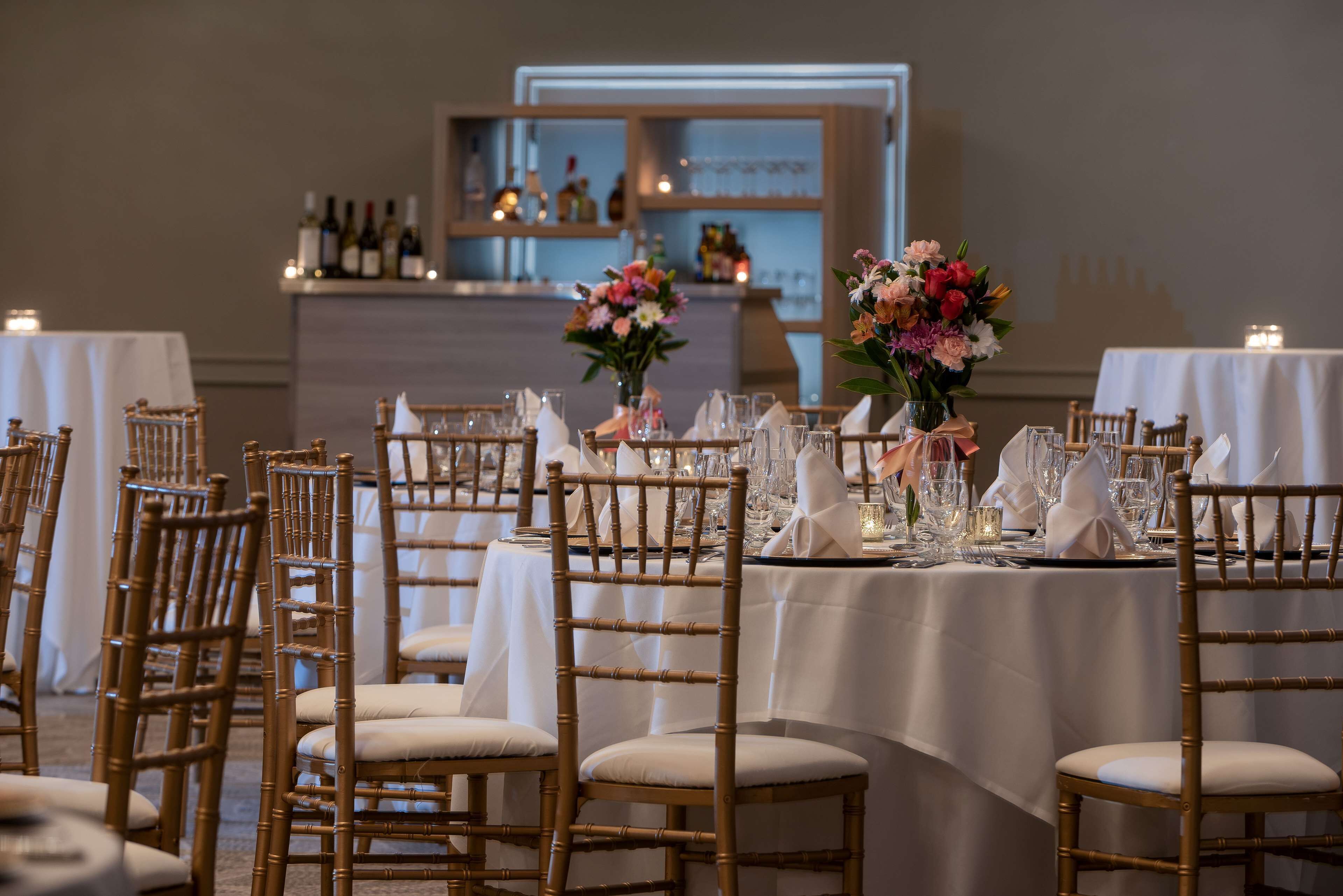 A banquet hall with round tables set for a formal event, featuring white tablecloths and gold chairs.