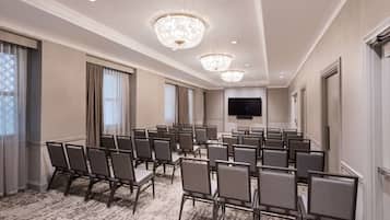A conference room with rows of chairs, a chandelier, a flat-screen TV, and a carpeted floor.