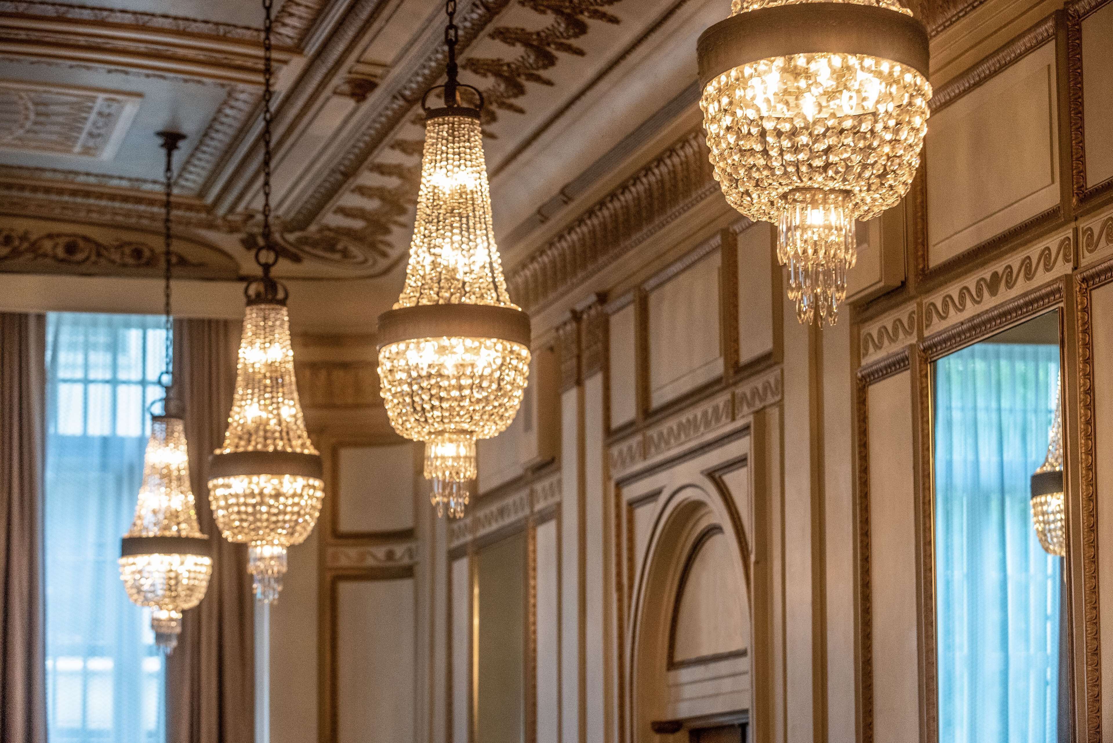 A grand hallway with ornate chandeliers, detailed wall moldings, and large windows.