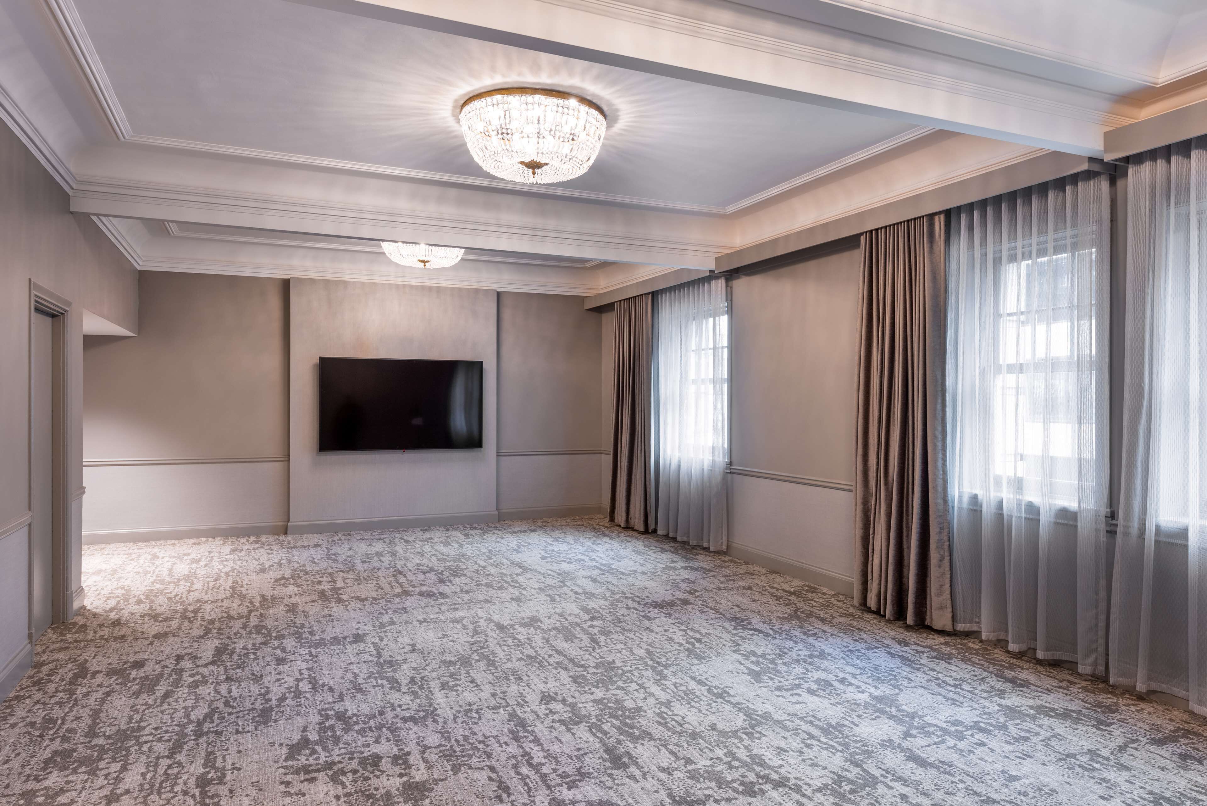 A spacious room with a large chandelier, a flat-screen TV, and heavy drapes.