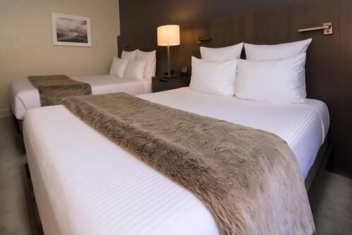 A hotel room with two beds, a nightstand with a lamp, and a framed picture on the wall.