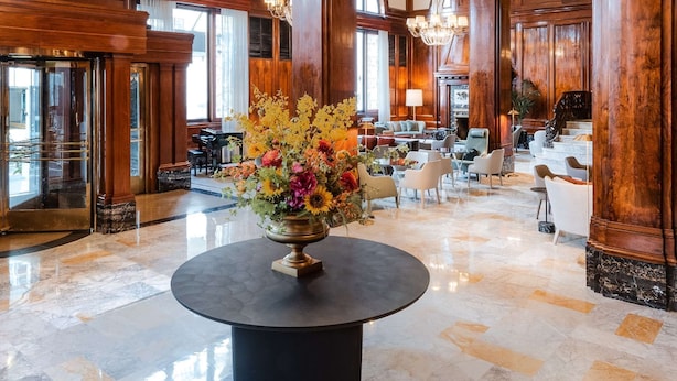 Un hall d’entrée spacieux, agrémenté d’un grand lustre, de boiseries et d’un arrangement floral central disposé sur une table ronde.