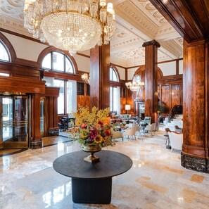 Un hall d’entrée spacieux, agrémenté d’un grand lustre, de boiseries et d’un arrangement floral central disposé sur une table ronde.