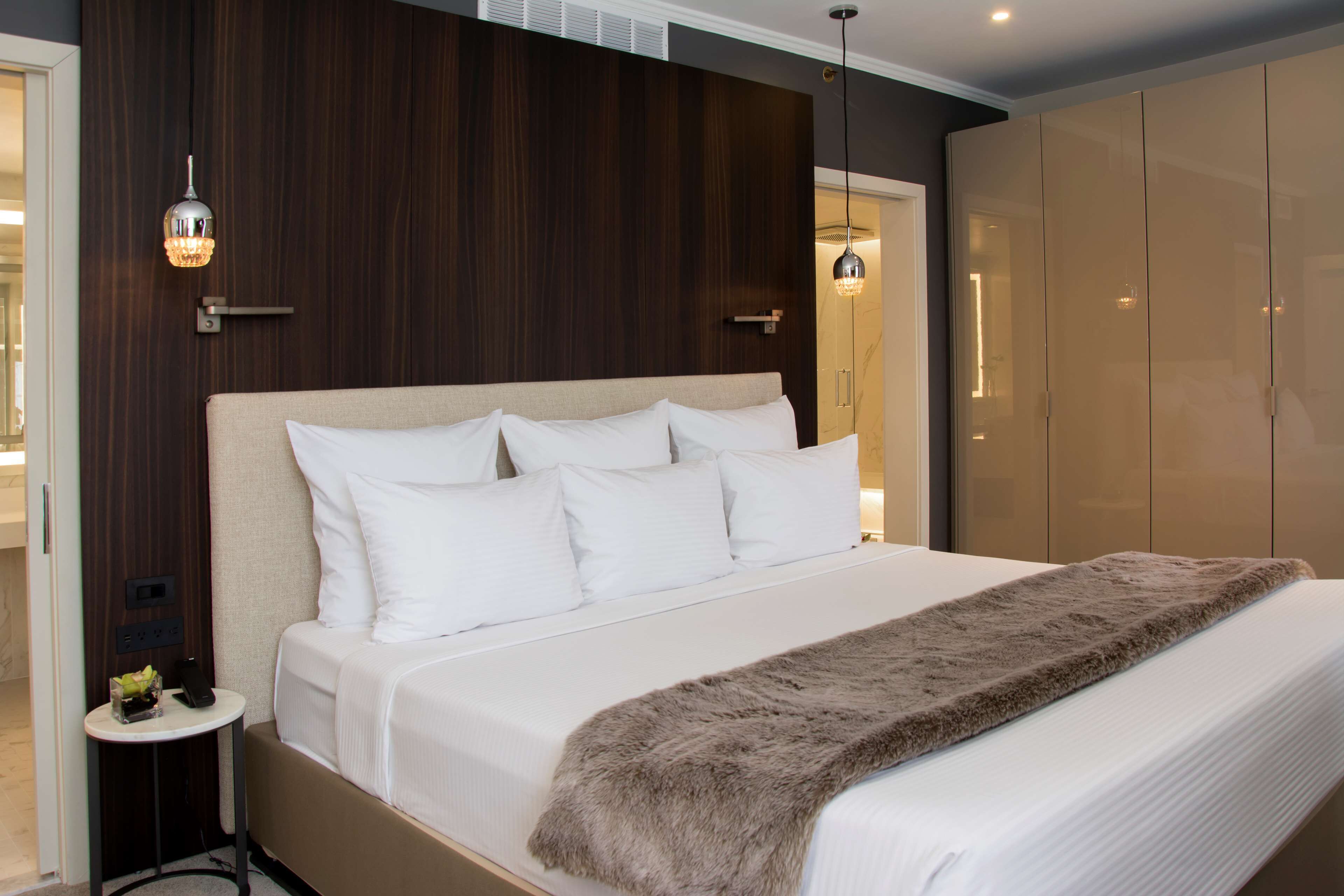 Una habitación de hotel moderna con una cama grande, una mesita de noche pequeña, un armario y una lámpara colgante.