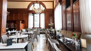 Un vaste espace dédié à la salle à manger, agrémenté de boiseries hautes, d’un lustre et de différents types de sièges, notamment des tables et des banquettes.
