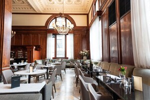 Un vaste espace dédié à la salle à manger, agrémenté de boiseries hautes, d’un lustre et de différents types de sièges, notamment des tables et des banquettes.
