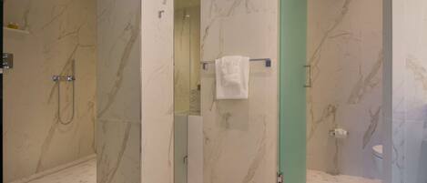 A modern bathroom with marble walls, a glass-enclosed shower, and a toilet with a towel rack.