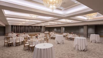 A banquet hall with round tables, white tablecloths, and gold chairs.