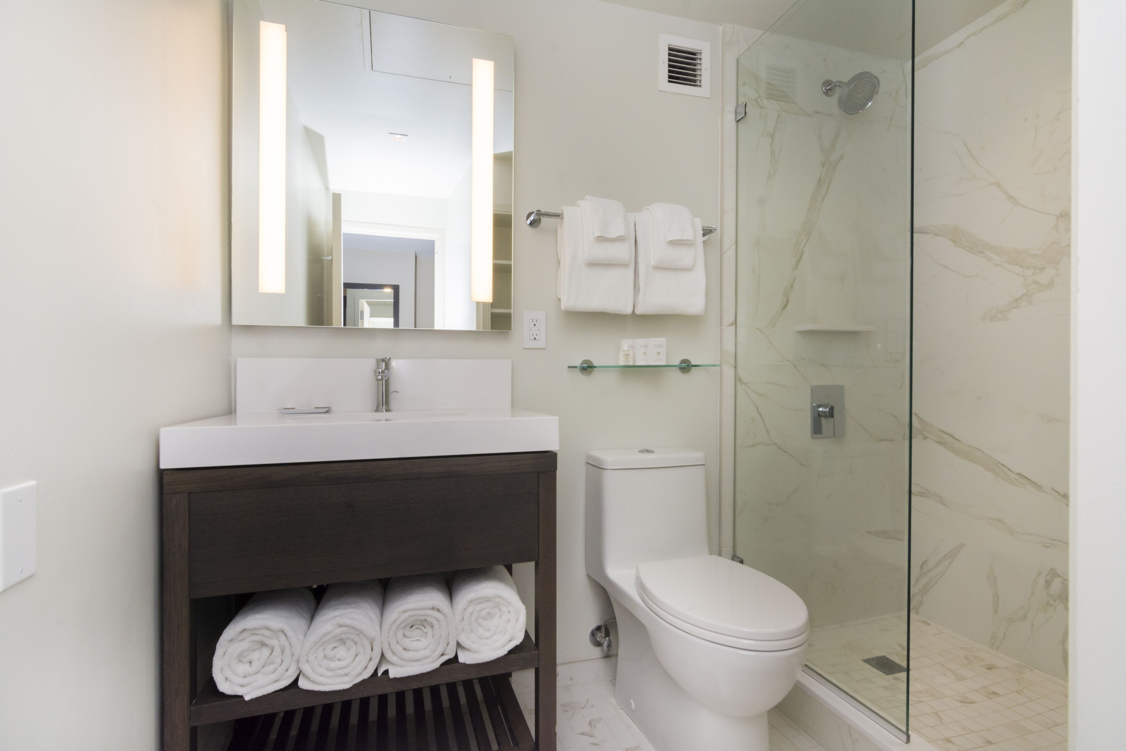 A modern bathroom with a white sink, a mirror, a toilet, and a glass-enclosed shower.
