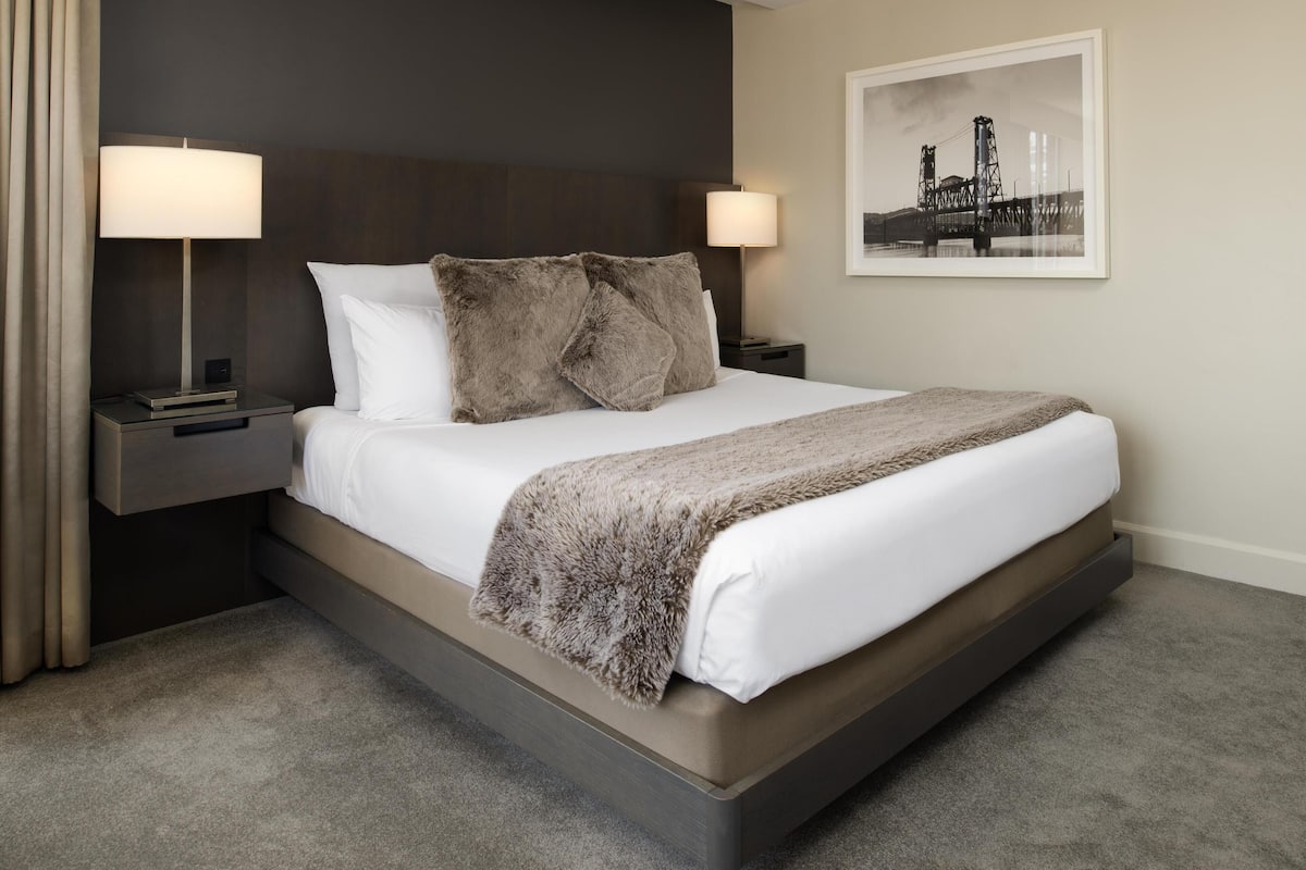 A hotel room with a large bed, two bedside lamps, a framed picture on the wall, and a carpeted floor.