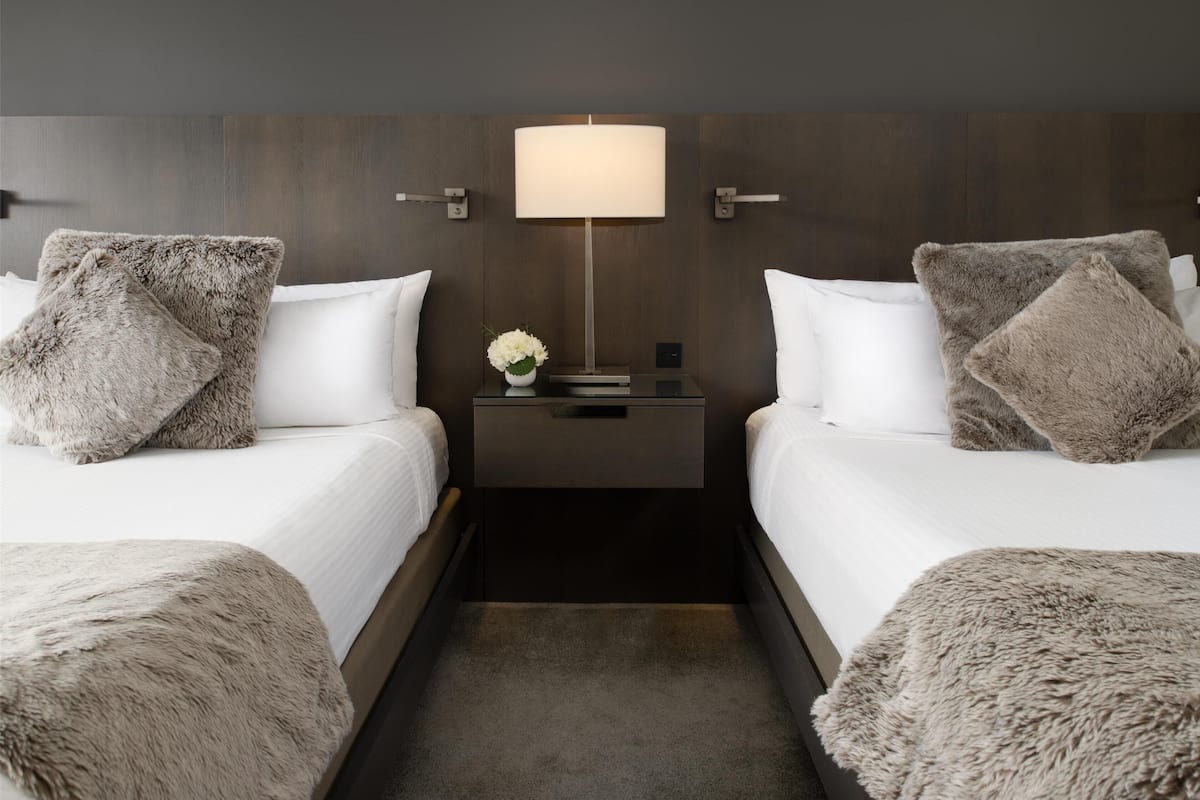 A hotel room with two beds, a nightstand with a lamp, and a vase with flowers.