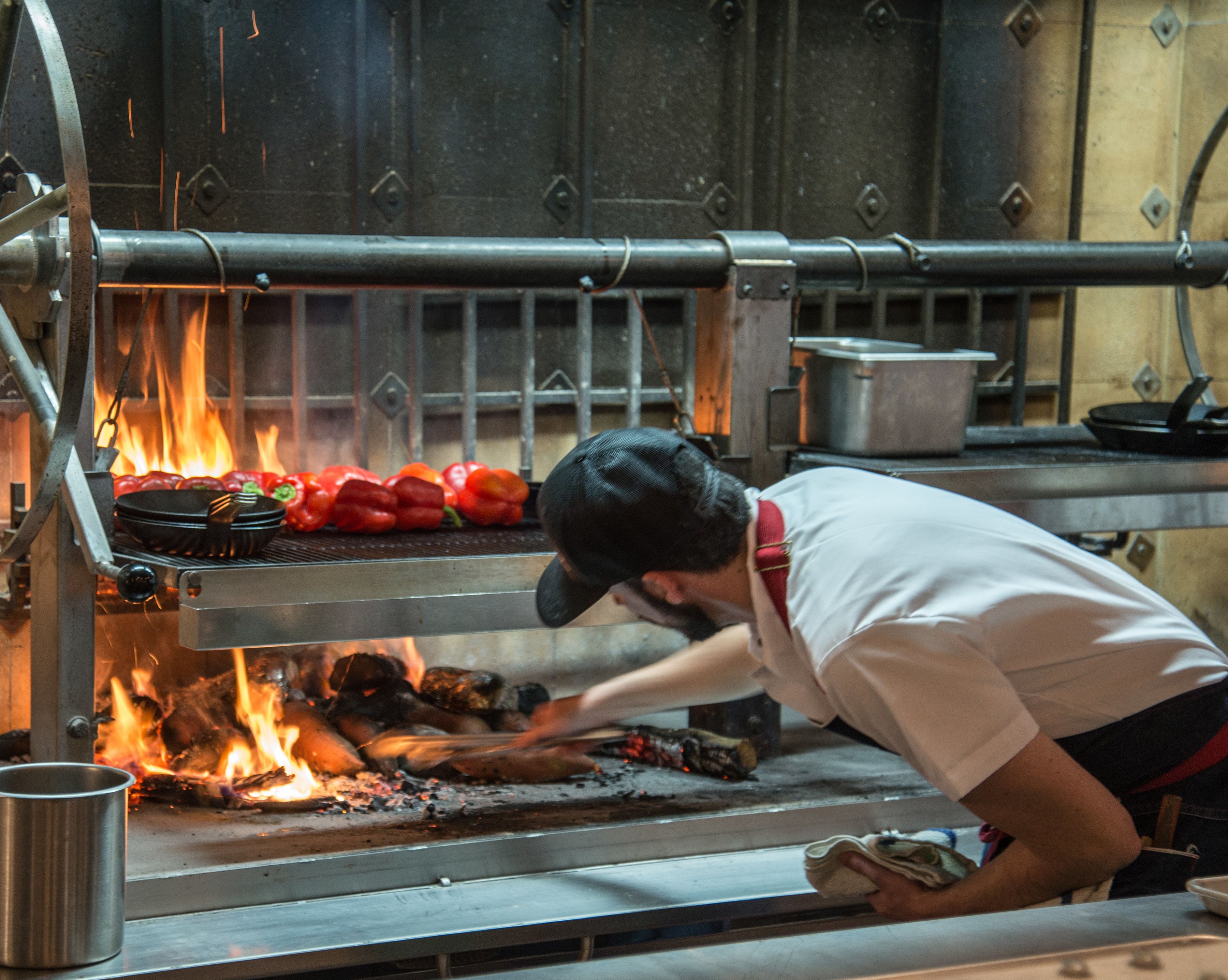 A chef cooking with a grill and a fire visible in the background.
