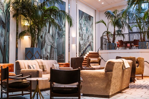 A spacious lobby with a modern design, featuring a large sofa, multiple chairs, a staircase, and large wall murals. - Hotel Theodore Seattle Downtown, Tapestry by Hilton (Seattle)