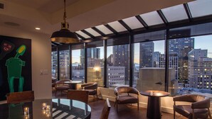 A modern dining area with a large table and chairs, large windows with a city view, and a unique green sculpture on the wall. - Hotel Theodore Seattle Downtown, Tapestry by Hilton (Seattle)