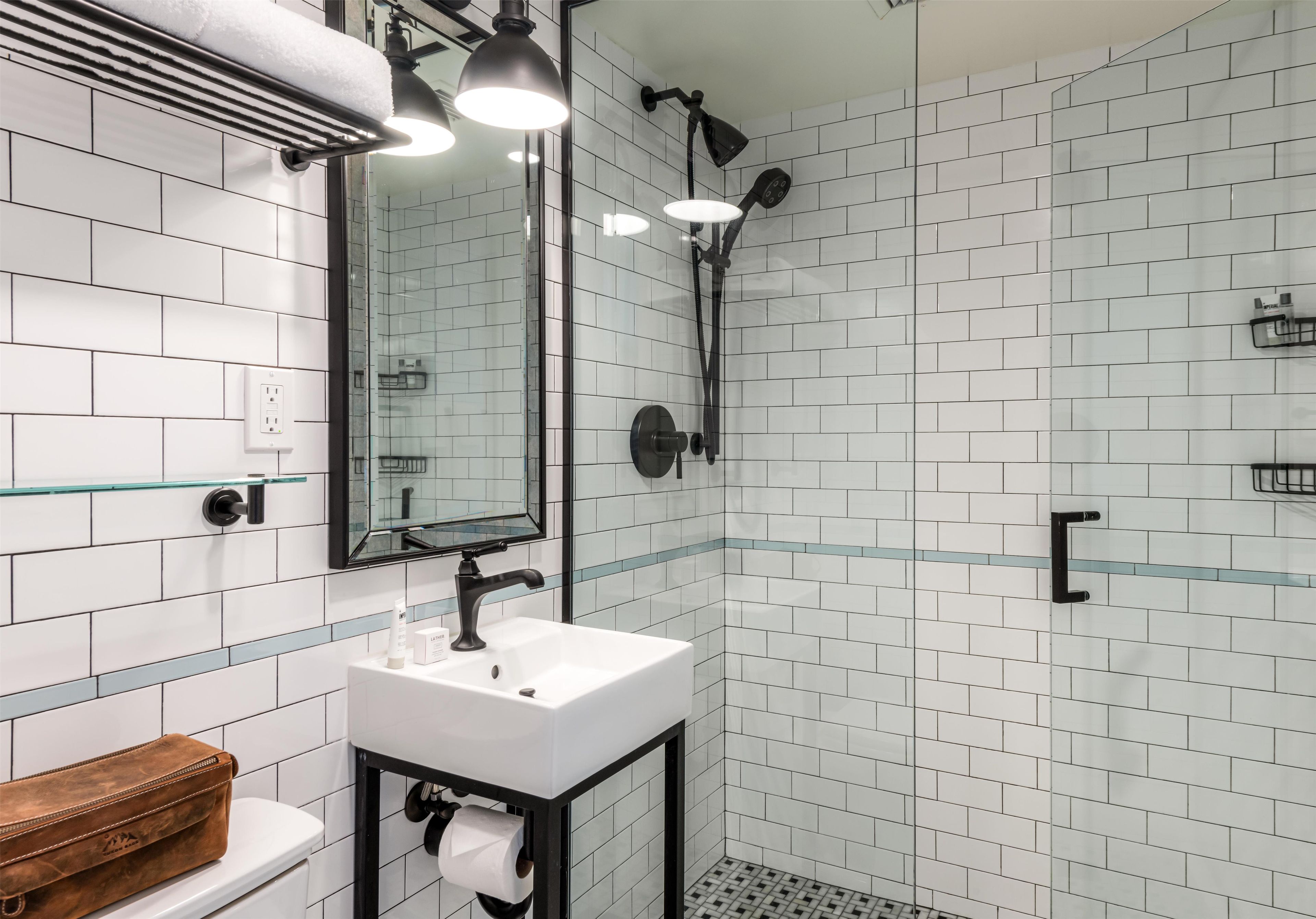 A modern bathroom with a white tiled shower, a glass shelf, and a wooden vanity.