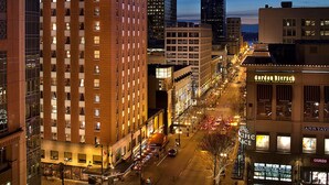 A high-rise hotel with a prominent name sign, a street view with cars, and illuminated buildings. - Hotel Theodore Seattle Downtown, Tapestry by Hilton (Seattle)