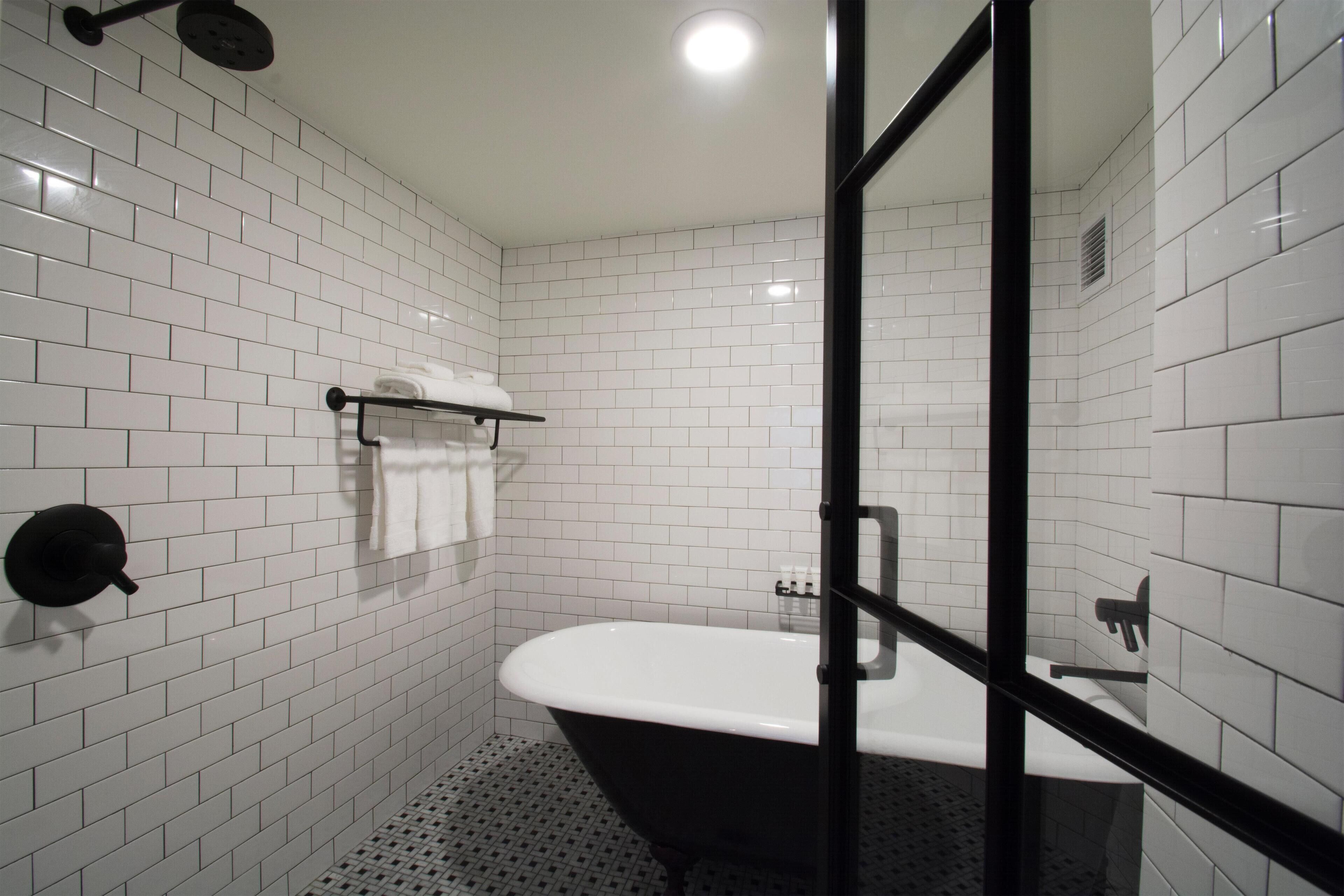 Une salle de bain moderne avec des carreaux de métro blancs, une baignoire noire et une cabine de douche en verre.